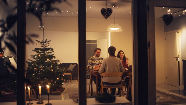 Familie spiser julemiddag juleaften i deres hjem, med julelys i vinduet og på juletræet.